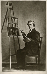 Porträttfoto av en ung man i mörk kavajkostym, som sitter fr