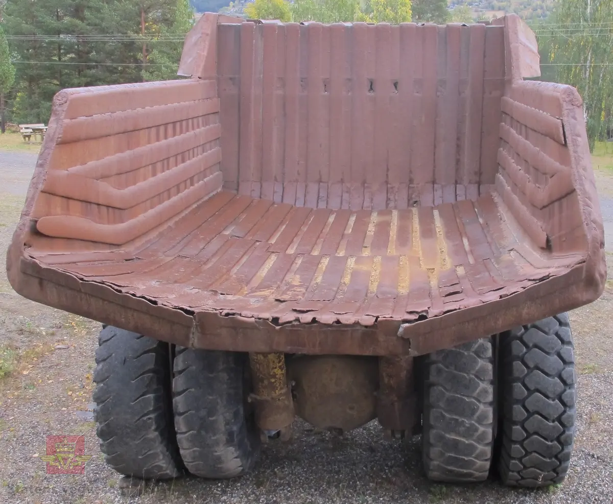 35 tonns gul dumper med 6 hjul, 2 akslinger. Tvillinghjul på bakaksel. 6-sylindret 14,6 liters Caterpillar dieselmotor som yter 400 hk. Dumperkassen har et volum på 17,8 m³. Skiltplater med serienummer 99F986 plassert på rammen og motoren. Metallplater fra produsenten med smørekart og advarsler. Hytte og motordeksler er i glassfiber. Dumperens toppfart er på 69 km/t.