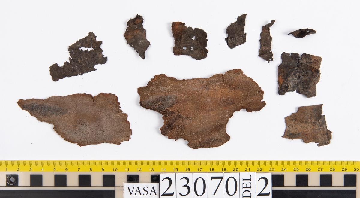 Sko.
Inuti skorna hittades även fragment från olika textilier som ursprungligen varit ett par strumpor. Idag sitter ett stickat fragment av ull fast i vänsterskon (23070) med avigsidan uppåt. I fyndet finns även en mängd lösa stickade fragment som idag är mycket korroderade och vissa helt mineraliserade av järn vilket har gjort textilen stenhård och därmed oerhört skör (23070a-c). Utifrån minskningar som några små fragment har så har det varit möjligt att rekonstruera strumpans tå. Genom att pussla ihop fragmenten som ursprungligen har suttit ihop har det på så vis gått att avgöra hur strumpans tå har varit konstruerad. Då textilen är så fragmentarisk är det inte möjligt att avgöra hur resten av strumpan har sett ut eller varit konstruerad. Däremot så finns det fragment av ett kypertvävt tyg av ull som på vissa ställen ligger dubbelt med det stickade 23070c). Ett av dessa fragment har stelnat i formen så som den suttit på fotens främre del inuti skon. Detta fragment täcker delvis det stickade tyget och har dessutom spår av kaststygn längs en kant. Så som det vävda tyget är placerat på det stickade tyget pekar på att man använt det som lagningslappar till sina stickade strumpor. 
I fyndet finns det även korroderade järnklumpar, ett tuskaftsvävt tyg av ull och rester av ett grovt bastfibergarn och två mindre läderfragment (23070d-f). Det är möjligt att även dessa har tillhört strumpan och/eller skon.

För mer detaljerad information från textildokumentationen (år 2022) se länkade filer.

Skodokumentation 2022:
Ovanläder. Tillverkad i getskinn av god kvalitet. Hör ihop med fyndnummer 23069 (Yngves skor). Tillverkades på en rak läst och bars på vänster fot. Inga dekorationer Det finns stygnhål som visar att det funnits invändiga förstärkningar (men förstärkningslappen saknas). Det finns delaminering men inga lagningar.
För mer information, se Länkade filer: Uppritning

Text in english:
This is the upper of a shoe of more “extreme fashion”, made of goatskin leather of good quality, probably made on a straight last and worn of the left foot, with no decorative features. The upper couples with 23069, together composing Yngve’s shoes. There are internal reinforcements missing from the upper and delamination, there are no repairs.
For more information, go to Länkade filer: Uppritning