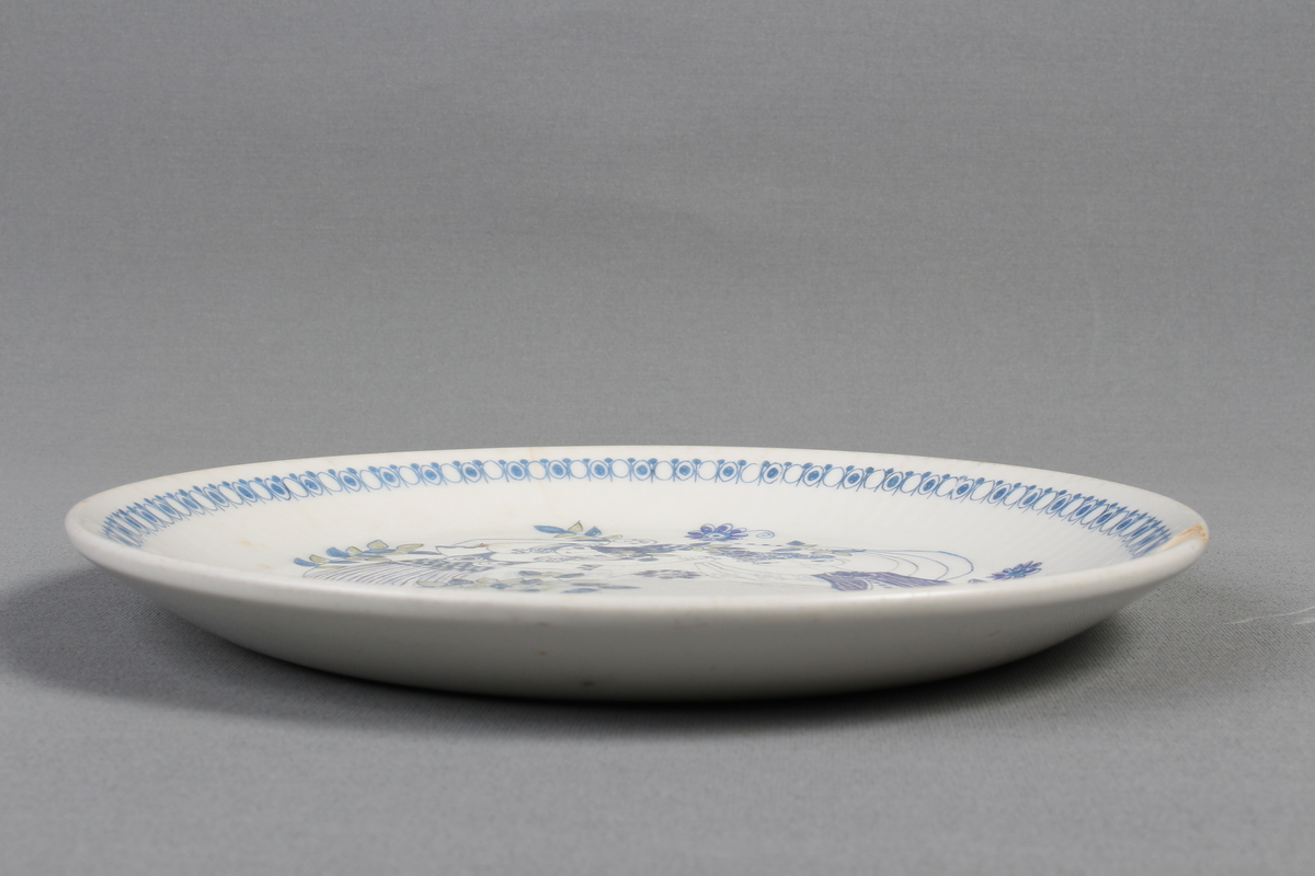 Tallerkene er dekorert med et bilde av en mann  og en kvinne som har blader og blomster på seg og rundt seg. De to menneskene er glade og de danser i blader og blomster.