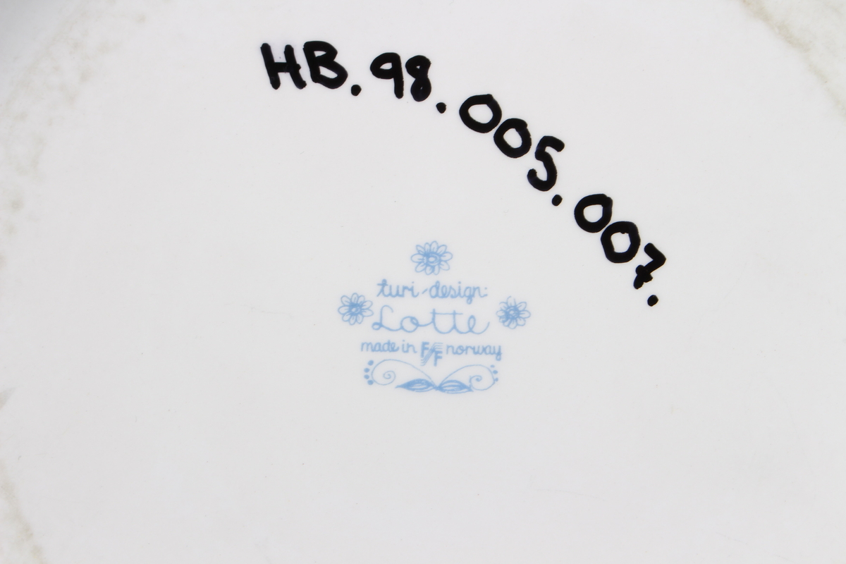 Tallerkene er dekorert med et bilde av en mann  og en kvinne som har blader og blomster på seg og rundt seg. De to menneskene er glade og de danser i blader og blomster.