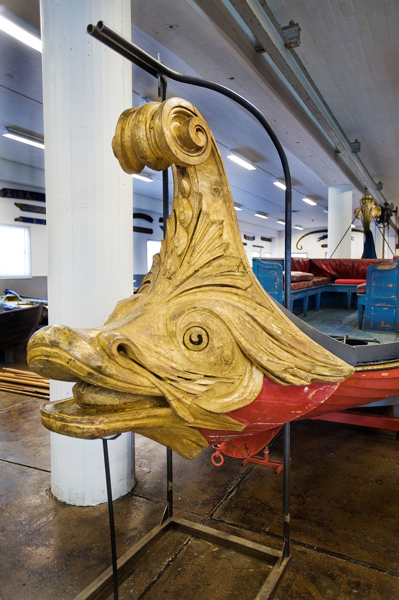 In 1783 King Gustaf III travelled to Italy. In Venice he was taken on a tour in a gold-ornamented gallery. The king also watched a splendid spectacle in the form of a regatta on the Canal Grande. A great number of decorated boats and gondolas assembled well before noon. At two o'clock in the afternoon boats with Venetian nobelmen came to pick up the king and his entourage to see the regatta. The boats were decorated with silk, canopies, parasols and flowers. The rowers were dressed in silk and adorned with silver. "The spectacel was vivid, full of splendor and distinctive character and quite dazzling", as Gundmund Jöran Adlerbeth writes in his diary from the journet. King Gustav III was very much impressed.

I order to supreise the king, master ship builder Fredrik Henrik af Chapman had "two pleasure vessels for Haga" built. Haga was a rural ground, north of Stockholm, where Gustav III at the time was creating a royal rank park. The "gondolas" were probably built in 1785 or 1786, and the heads of the boats were in all certainty made by the sculptor Hohan Törnström.

The king was "infinitley pleased", and the sloops came to be used frequently on the Brunnsviken and off Drottningholm. For rowing, boatsmen commandeered from the navy were used. The boar have been called sloops, pleasure vessels or gondolas depending on where they mentioned. The shields were originally 24 in number, with motifs from antiquity and from the twelve labors of Heracles.

After the assassination of Gustav III the sloops were forgotten and rarley used until they were pun into service again for a while during the reign of Karl XV (1859-1872). Since then, they have been stored at various places, e g near the copper tents at Haga, on Skeppsholmen and, since 1966, in the collections of the National Maritime Museum.    