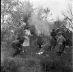 Barn och vuxna samlade runt en eld för korvgrillning. Några ryggar för röken. Det är gökotta, möjligen i Gränna Lions regi. De vuxna till vänster är Sture Petri och Margit Antonsson.