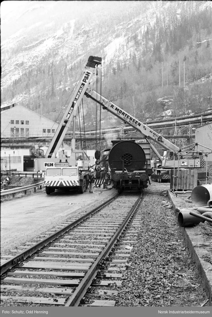 En 70 - tonns dampkjele flyttes fra jernbanevogn til trailer ved hjelp av to kranbiler.