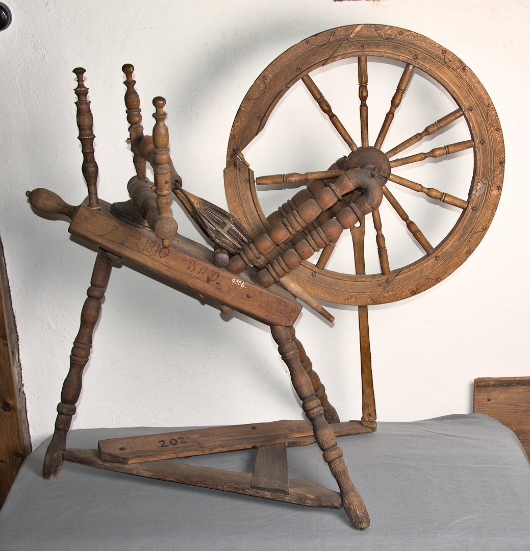 Spinnrock av trä med axel av järn och lager för rullen av läder. Snedställt bröst. Hjulet vilar på dubbla stöd. Inbrända stjärnmönster och bågar på bröst och hjul. Mått: hjulets diameter 29,3 cm, hjullötens djup 6,4 cm. 
