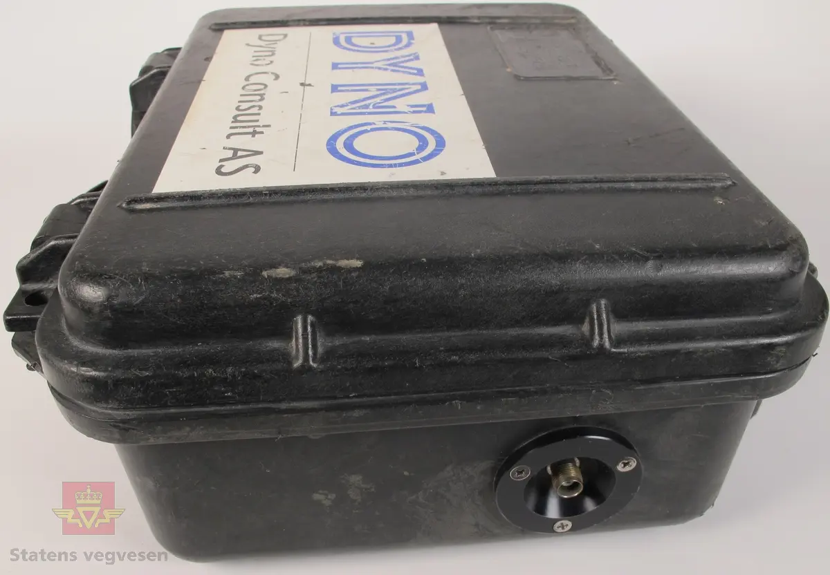 Svart koffert i plast som inneholder vibrasjonsmåler. Kofferten har bærehåndtak og to lukkemekanismer, samt mulighet for å låse med hengelås. Innskriften Peli-Case Pelican Products Inc, Torrance, CA Made in U.S.A, tre klistremerker med påskriften 236, og et klistremerke med påskriften DYNO Dyno Consult AS. Innvendig i kofferten er det en plate med bruksanvisning, samt selve vibrasjonsmåleren med skjerm, knapper og lesevindu. Påskriften Nitro Consult UVS 1201 Vibration Monitor samt klistrermerker med påskriftene 236, NB! DISPLAY ON VED START/STOPP, DYNO Dyno Consult AS Gullhaug Postboks 614 3412 Lierstranda Telefon: 32 84 12 00 Telefax: 32 22 81 83 og BJARNE FOSS. På siden av kofferten er det tilkoblingspunkt for ledning. Medfølgende batteri med påskriften Hellesens GOLD 855 4R25 6 VOLT.