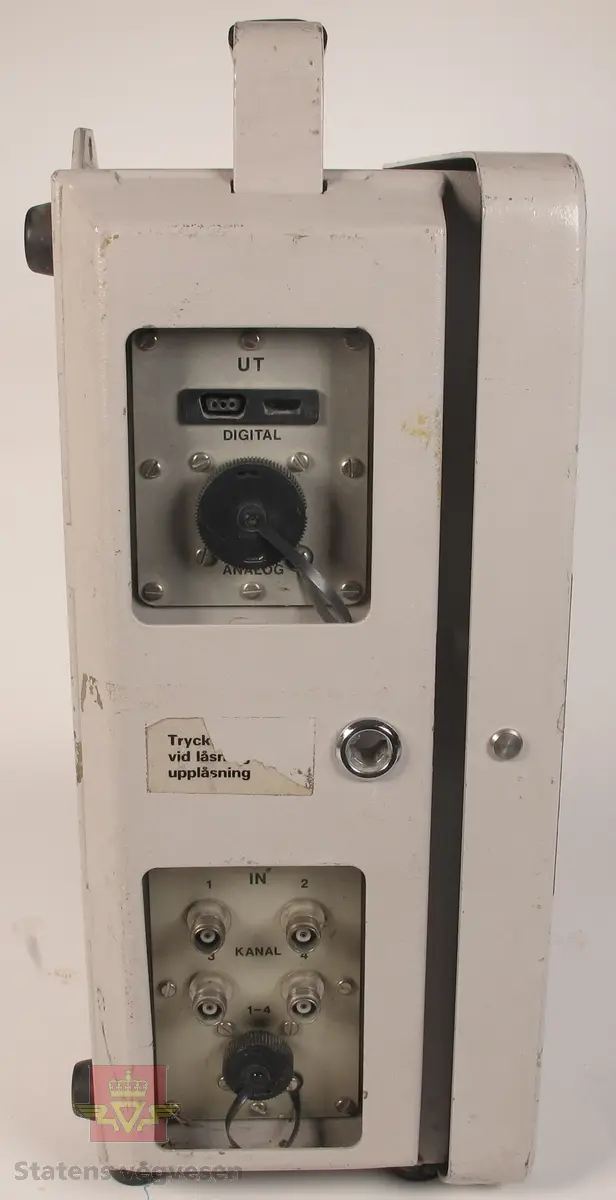 Vibrasjonsmåler UVS 1404. Grålakkert skap i metall som inneholder en vibrasjonsmåler. Bærehåndtak med lær på toppen, fire gummiføtter for stående bruk og fire gummiføtter for liggende bruk, samt brakett for opphenging vertikalt. Lås på skapdør og en lås på nedre del av betjeningspanelet. Utsiden av skapet har påskriftene UVS 1404 Vibration Monitor Nitro Consult fra produsenten, samt klistremerker med påskriftene DYNO Dyno Consult AS Gullaug Postboks 614 3412 LIERSTRANDA Telf: 32 84 12 00 Telefax: 32 22 81 83, TRYKK LOKK INNTIL VED ÅPNING/LUKKING, 051 og 0051. Skiltplate med innskriften Nitro Consult UVS 1404 Vibration Monitor Ser.no. 0051 Made in Sweden på siden av skapet. Vibrasjonsmåleren har påskriften UVS 1404 Vibration Monitor Nitro Consult fra produsenten, og klistremerker med påskriftene DYNO Dyno Consult AS Gullaug Postboks 614 3412 LIERSTRANDA Telefon: 32 84 12 00 Telefax: 32 22 81 83 og AVLESNING SE INNSIDEN AV LOKK. Vibrasjonsmåleren har to betjeningspanel, det ene under låsbart lokk og avlesningsvinduer. På siden av skapet er det tilkoblingsmuligheter for kabler. 2 stk 6 volts batterier med påskriften DURACELL PROCELL PROFFESIONAL ALKALINE BATTERY PC908 6 VOLT BEST IF INSTALLED BY: JAN 2002.