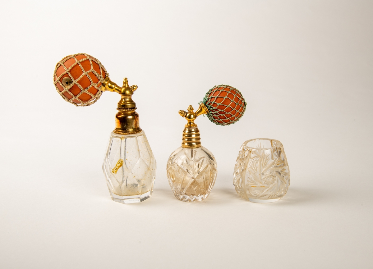 Flakonger i fasettslepet krystall med forgylte topper. Rød gummiballong i grønt trådnett.  Ligger i en såpeeske. Høyde på flakongene: 12 og 10 cm.