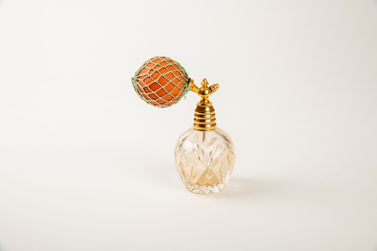 Flakonger i fasettslepet krystall med forgylte topper. Rød gummiballong i grønt trådnett.  Ligger i en såpeeske. Høyde på flakongene: 12 og 10 cm.