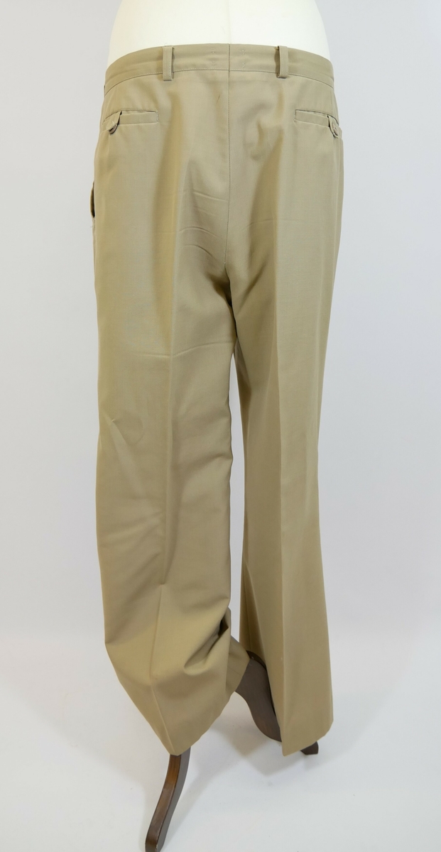 Brun bukse med press. Buksesmekk med glidelås og to metallhekter øverst. To lommer foran og to baklommer. 

Påskrift lapp inne i buksa: 
UNIFORM // STORMARK // Konfeksjonsfabrikk a/s // DOKKA