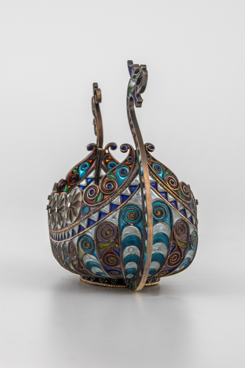 Pyntegjenstand, utformet som et vikingskip, i sølvfiligran og vindusemalje. Oval formet "kjøl" i sølv. Resten av båten er bygget opp av et intrikat filigransarbeid, hvor mellomrommene er fylt med transparent vindusemalje i ulike farger. Filigranstrådene danner rosettformede skjold langs skipets relling, samt voluttornmaenter og s-former på korpus. Forstevnen er utformet som et gapende dragehode, mens akterstaven har avsluttes med blomsterornamenter.