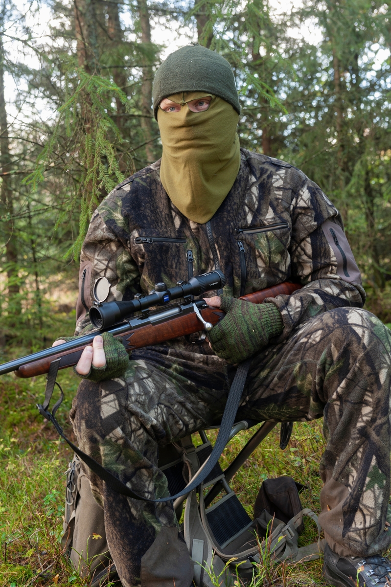 Jeger på post under høstjakta. Posten er plassert nær der man tror viltet kommer, gjerne nær dyrestier eller kjente trekkruter for viltet. Posten er plasseert i tett skog med fri sikt mot åpent terreng. Jegeren bruker en lydløs smygdress av merket Swedish Chasseur Predator Ursus som er utviklet av Rasmus Boström og Jonas Lännbjer. Det finnes også kamuflasjedrakter fra andre produsenter på markedet. Når det er mildt om høsten er det vanlig å sitte uten ansiktsmaske. Jegeren er utstyrt med børse. Han har med seg en jaktradio og Garmin GPS. Jeger: Jan Ove Fuglebrenden fra Løten. Bildet er arrangert. 