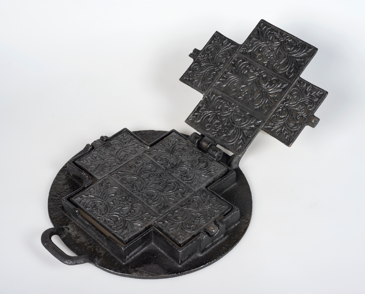 Kakejern med stativ. Jernet er forma som et likearma kryss og kan romme fem kaker om gangen. Stativet er rundt.