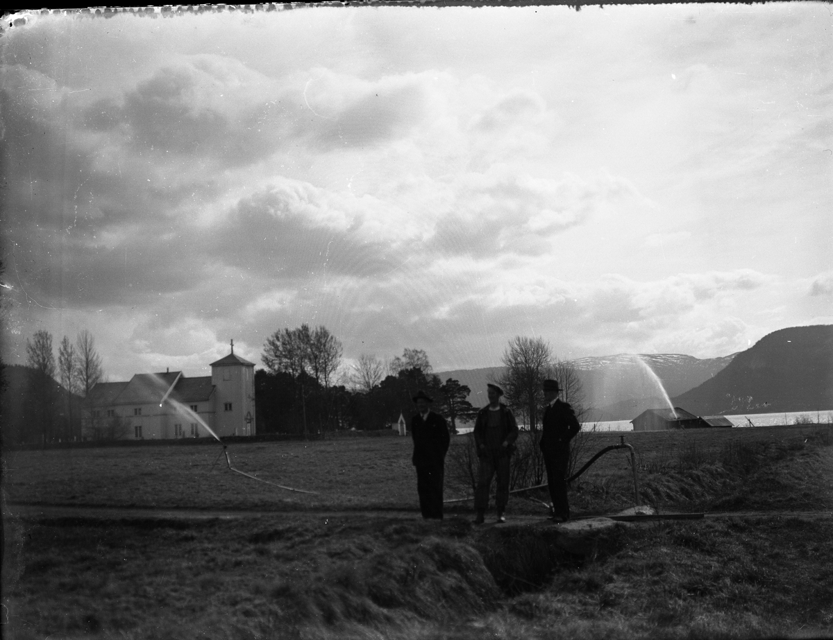 Fotosamling etter Bendik Ketilson Taraldlien (1863-1951) Fyresdal. Gårdbruker, fotograf og skogbruksmann. Fotosamlingen etter fotograf Taraldlien dokumenterer områdene Fyresdal og omegn. 
Motiv med Moland Kirke. Vanning sees på prestegården.