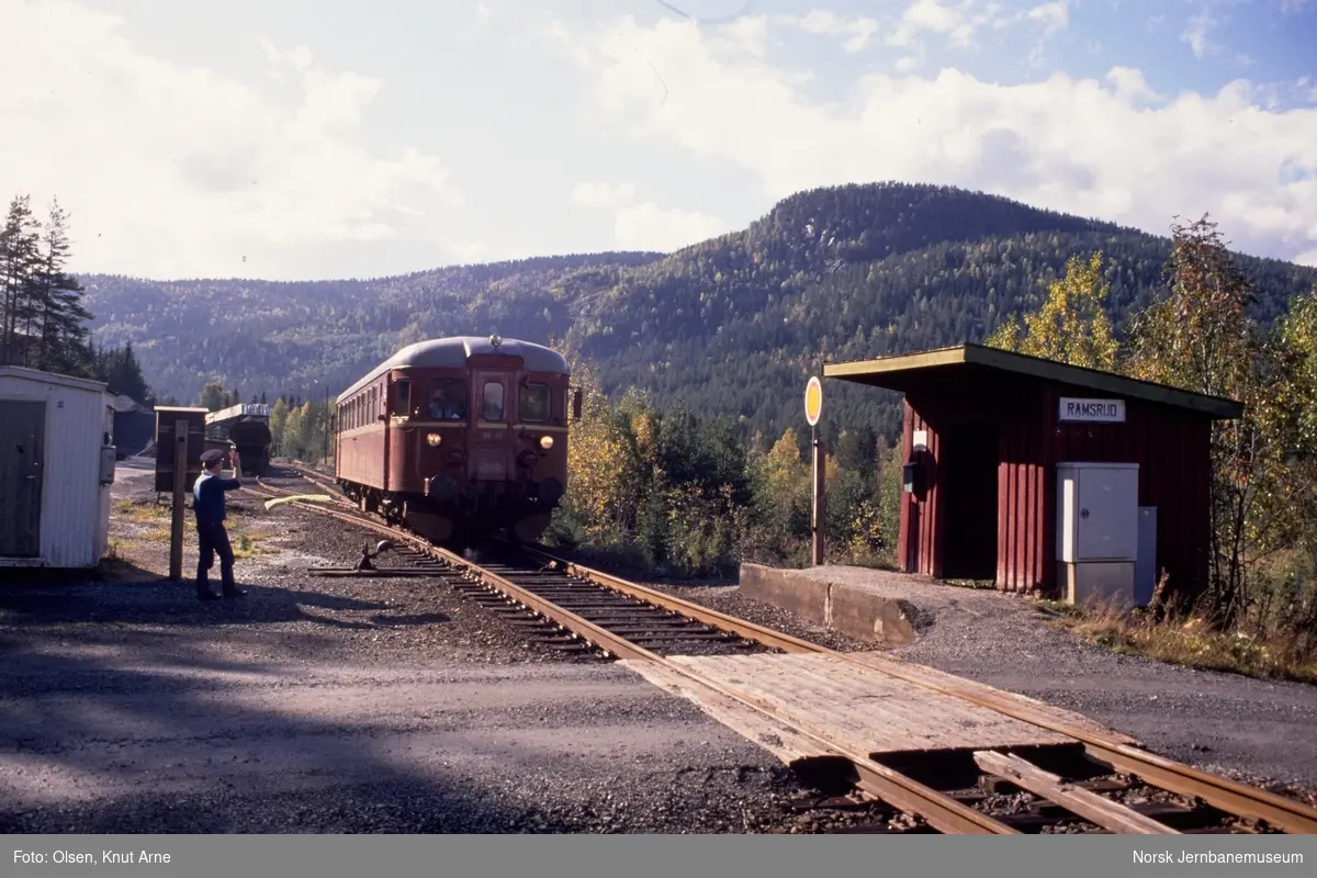 Ramsrud holdeplass er opprettet midlertidig stasjon med signalsted ved sidesporet, og togekspeditør Karsten Brodal viser grønt flagg. Denne løsningen ble benyttet ved arbeider på banen. I bakgrunnen dieselmotorvogn BM 86 25 med persontog fra Kongsberg til Rødberg