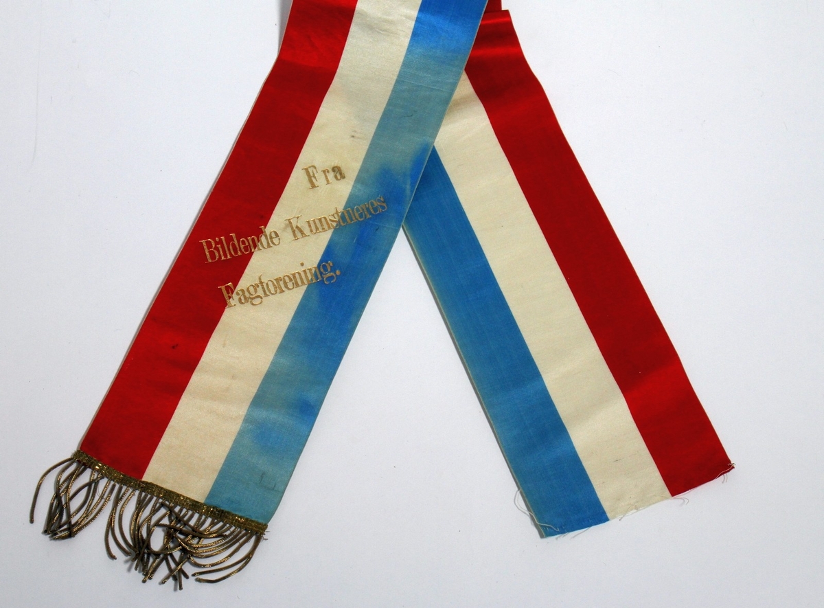 Båresløyfe frå Ivar Aasen si gravferd i 1896. Aasen døydde 23. september 1896, og det var gravferd frå Vår Frelsars gravlund 29. september. (1) På sløyfa står det ei helsing "Fra Bildende Kunstneres Fagforening".

Kjelde:
https://www.sprakradet.no/Vi-og-vart/Publikasjoner/Spraaknytt/Arkivet/Spraaknytt_1996/Spraaknytt_1996_1/Om_Ivar_Aasen_i_eit_minneaar/ (Lesedato: 15.10.2020)