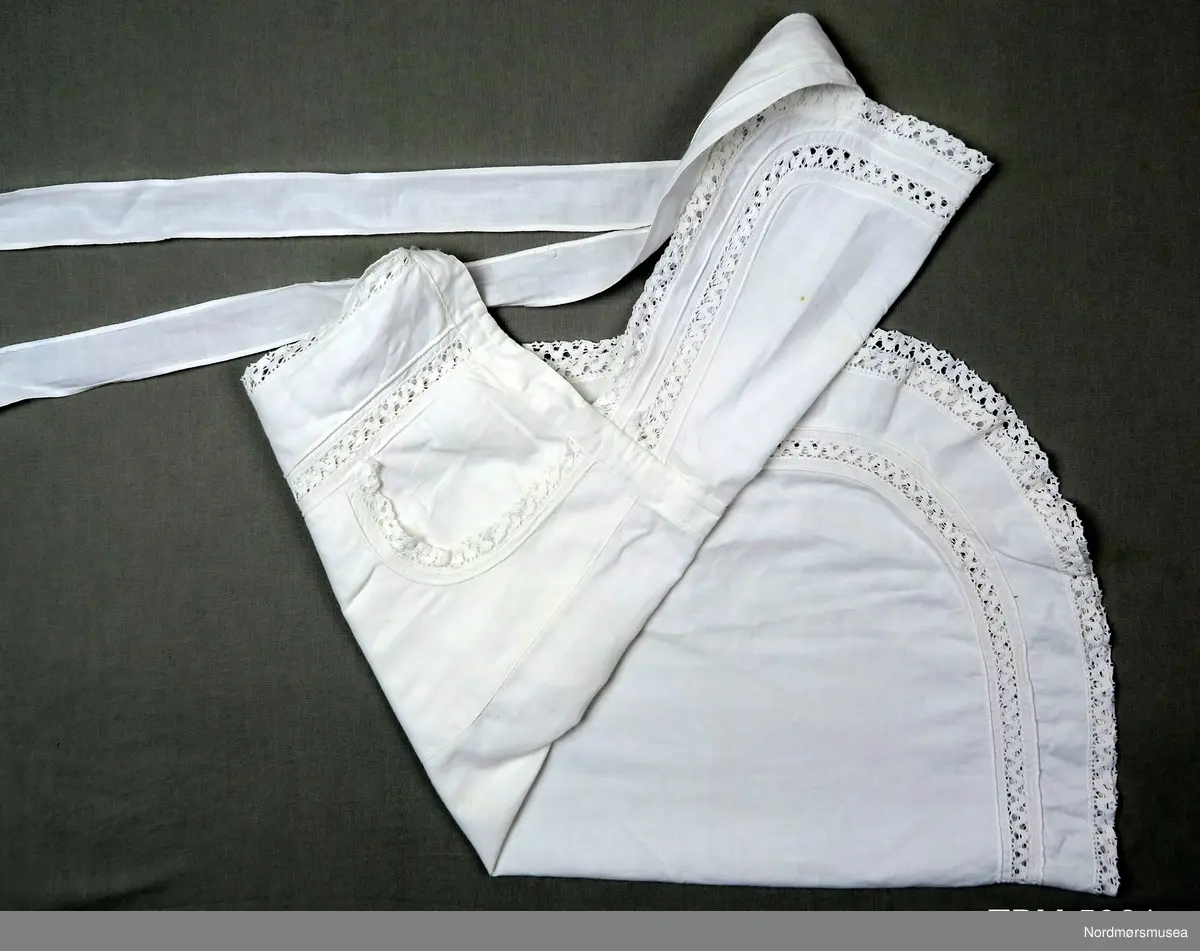 Rundt hele forkleet er det kanter av blonde. Blonder er også innfelt 4 cm inne på smekken og på sjølve forkleet.
To lommmer, også de har blonder. Sjølve forkleet er avrunda nederst.