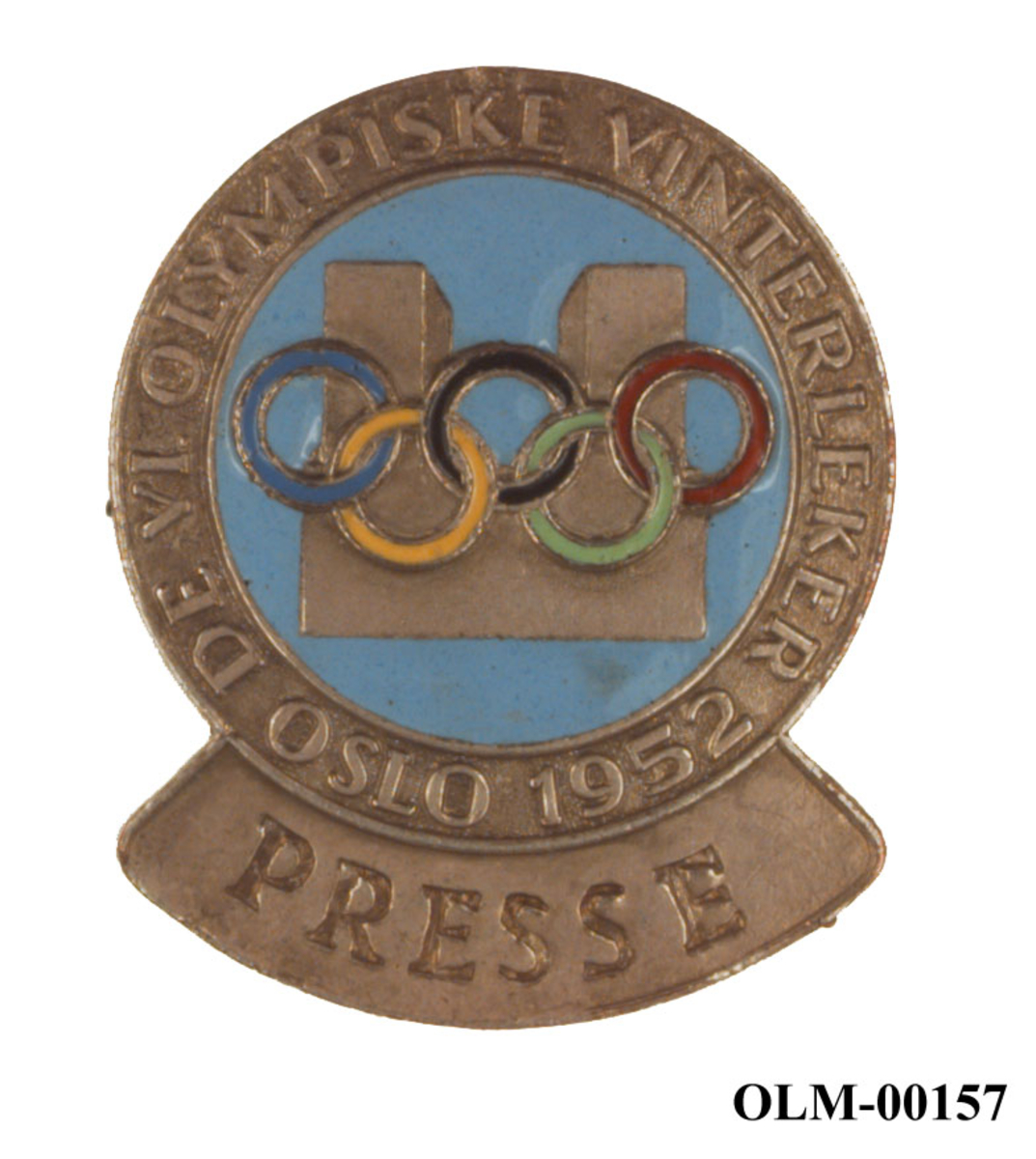 Merke av metall med logo for de olympiske vinterleker i Oslo i 1952. I logoen er det motiv av rådhuset i Oslo og de olympiske ringene.