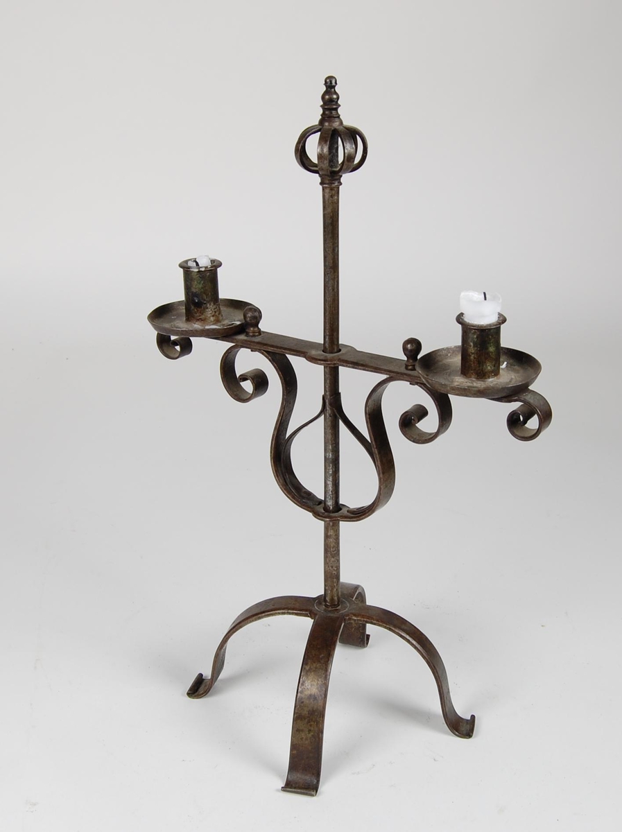 Staken er sammensatt av smidde deler, og består av en firbeint fot med en stang, toppet av en krone. På stangen er en lysarm med to lysholdere. Lysarmen er justerbar i høyden.