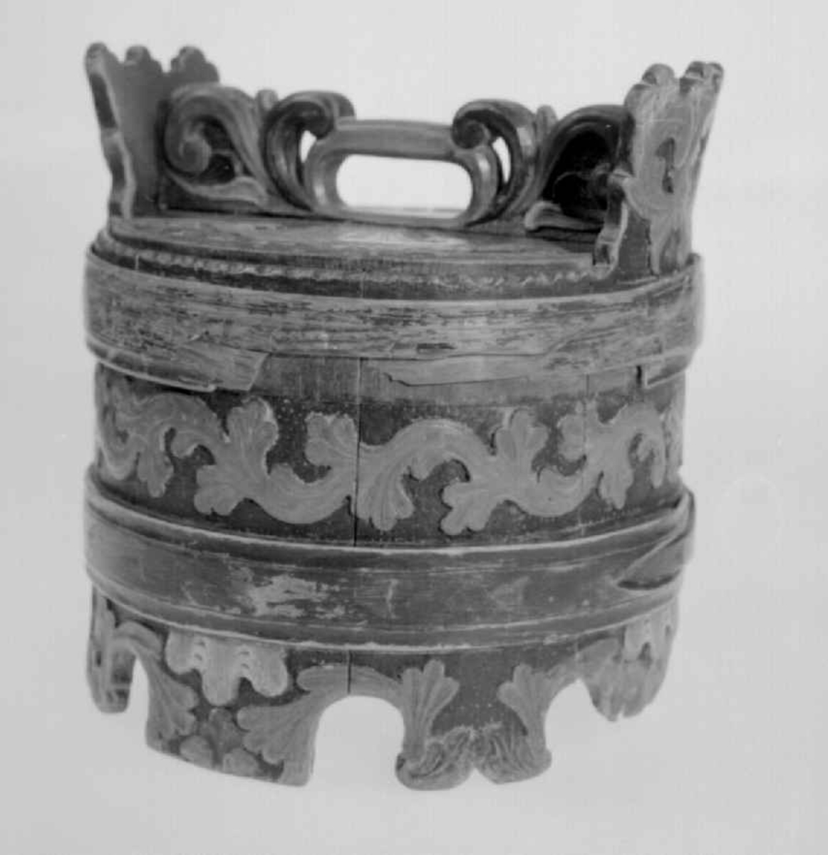 Grønnmalt ambar med to flate grønne gjorder. Mellom dem et felt med skåret og rødmalt akantusbord. Skåret og malt akantusmotiv på føttene - sju intakte og en defekt. Akantus skurd på ørene og skåret lokk med håndtak. Mangler stengsel for lokket. Påmalt innskrift som er slitt og uleselig på et av båndene. Skåret perlerad langs ene kanten.