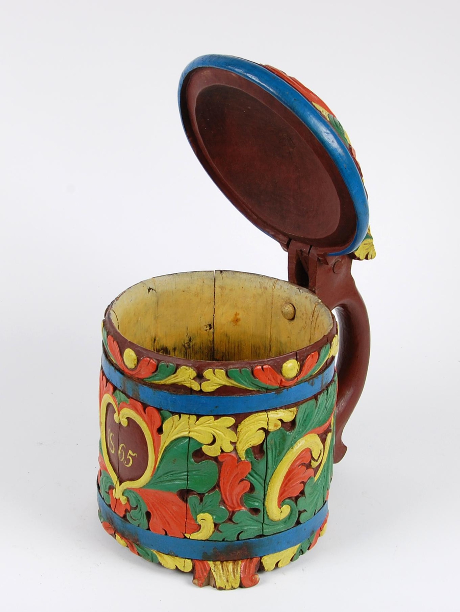 Kanne av staver. Lokk med gule, grønne og røde blader, blåmalt kant. Korpus med en blåmalt metallgjord oppe og nede, gule, grønne og røde akantusblader, brunmalt hjerteformet felt med innskriften 1865. Brunmalt hank. Tre røde og gule føtter.