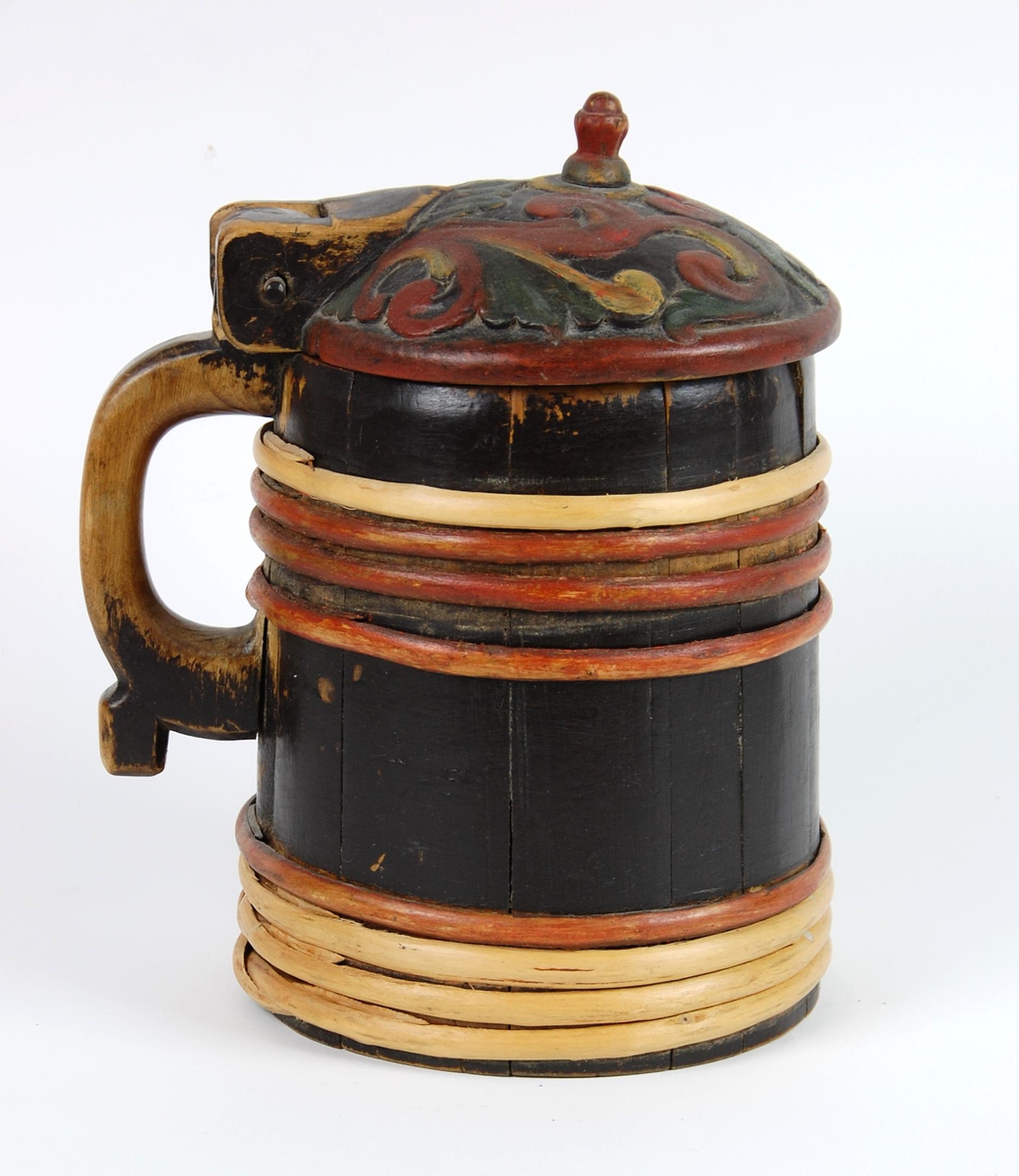 Kanne av trestaver. Lokk med rødt, gult og grønt akantusskurd. Korpus med fire gjorder oppe og nede, fire av gjordene er av nyere dato, sotmalet. hanken er skåret ut av en stav.