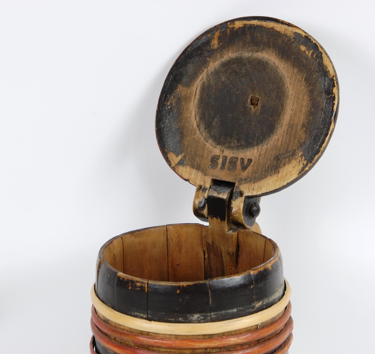 Kanne av trestaver. Lokk med rødt, gult og grønt akantusskurd. Korpus med fire gjorder oppe og nede, fire av gjordene er av nyere dato, sotmalet. hanken er skåret ut av en stav.