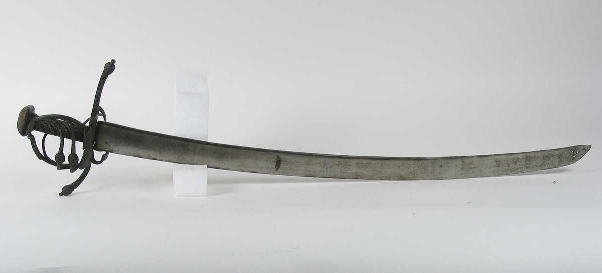 Pyramideformet knapp med strekdekor. Asymmetrisk kurvfeste med to sidebøyler( øverste avbrukket )med riflede fortykkelser på midten. mellom håndbøylen og kurvens ytterkant. Innsiden har en  sidebøyle. Kurvens basis er på utsiden en kvadratisk parérplate med to hjerteformede gjennombrytninger. På innsiden er det en klingebrekker og tommelbøyle. Opp og nedbøyde parérstenger med riflede fortykkelser på endene.
Tregrep med nyere jerntrådvikling.
Enegget krum klinge med 3 hull ipå klingspissen og en smal hulslipning på ryggsiden.Tre smedmerker på venstre side. 