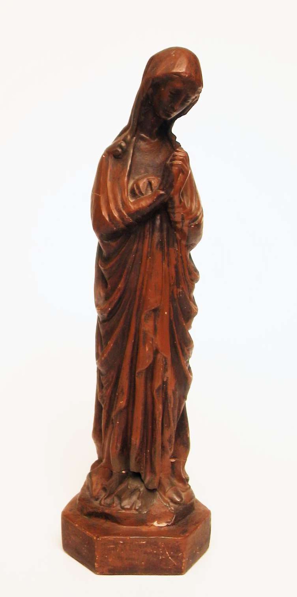 En skulptur av jomfru Maria støpt i gips og malt brun.
Skulpturen har vært slått i to og er limt sammen igjen.
