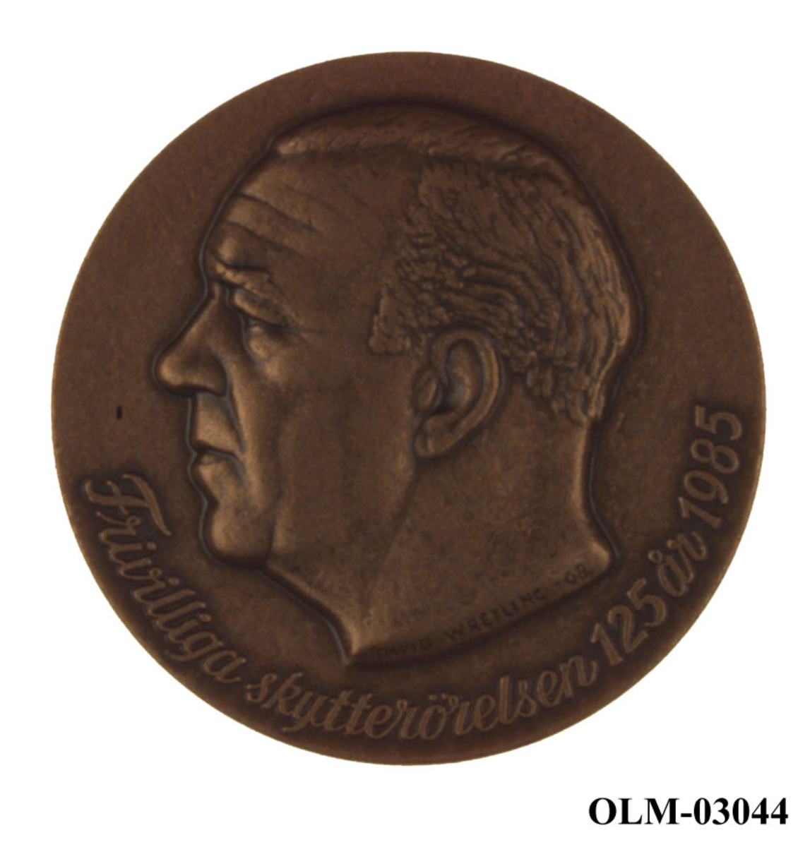 Bronsefarget medalje med motiv av et hode til en ukjent person. Hodet er i profil. Det er også motiv av det som antas å være emblemet til den Frivilliga skytterörelsen.