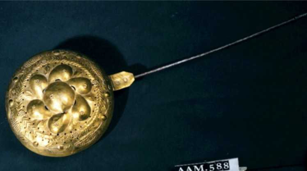 Sengevarmer.   messing.   Beholder rund. Lokk drevet med uthamrede ornament.  Under kanten jernring. Skaft jern.  Messing,   drevet, punslet og gjennombrutt arbeid,   innvendig fortinnet.  I lokket innvendig sees   kobber.  Midt på lokket en stor rund bule (eple?) med 6  pæreformete buler omkring, i mellomrommene mellom  pærene stiplete blad i lavere relieff. Langs kanten  en bladgren, ytterst med 4 kongleformer på gren med  blad. Sekskantet hengselbeslag med to messingnagler,  over det nederste utydelig stempel  Langt  jernskaft med to profilringer øverst.  På baksiden svakt synlige eierinitialer.  Skaftet går over i jernring rundt pannen., som har skrånende sider mot bunnen. RH.