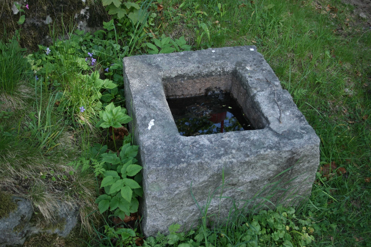 Rektangulær  steinblokk med et rektangulært forsenket vannkarl på toppen, ca. 15 cm  dypt. En smal avløpsrenne midt på den ene langsides karm.  Grovt  tilhugget overflate. 
