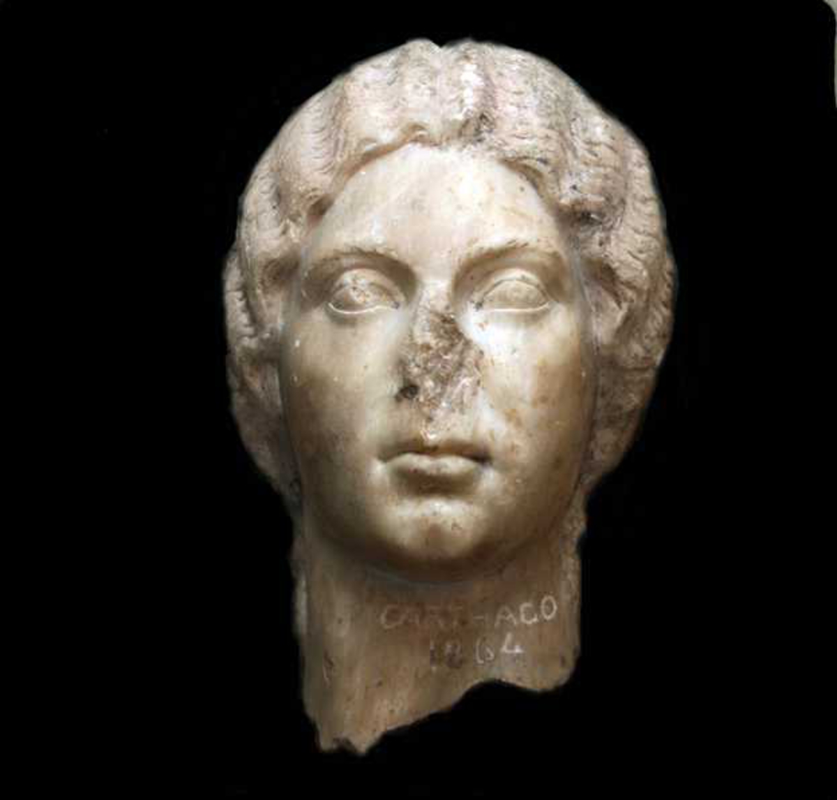 Portrett skultptur (del). Hodet er avbrukket et stykke ned på  halsen, med  ujevn bruddlinje, har antagelig tilhørt legemesstor statue.  Ansiktet er   ovalt,  med tunge fyldige trekk. Håret ligger som en tett hette  rundt  hodet, det er skilt i midten, bølger lett og samles bak i  en  stor knute. Løse lokker henger ned bak ørene. Øynene er  store,  med svulmende øyelokk og markert tårekanal. Øyebrynene er buskete  skravert. Munnen er bløt, med underleppen mest  fremtredende.