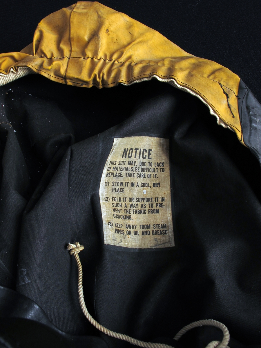 Gummidress, brukt av alliert marine og handelsflåte under krigen 1940 - 45. 
Sort dress med gul hette. Stor gummiddress med påsatte støvler, som har blyinnlegg for å holde drakten flytende loddrett. Lange ermer, vid halsåpning med snoretrekk og gul hette med innvendig hvit elastikk. Innv. bruksanvisning.  Stempel under sålen.