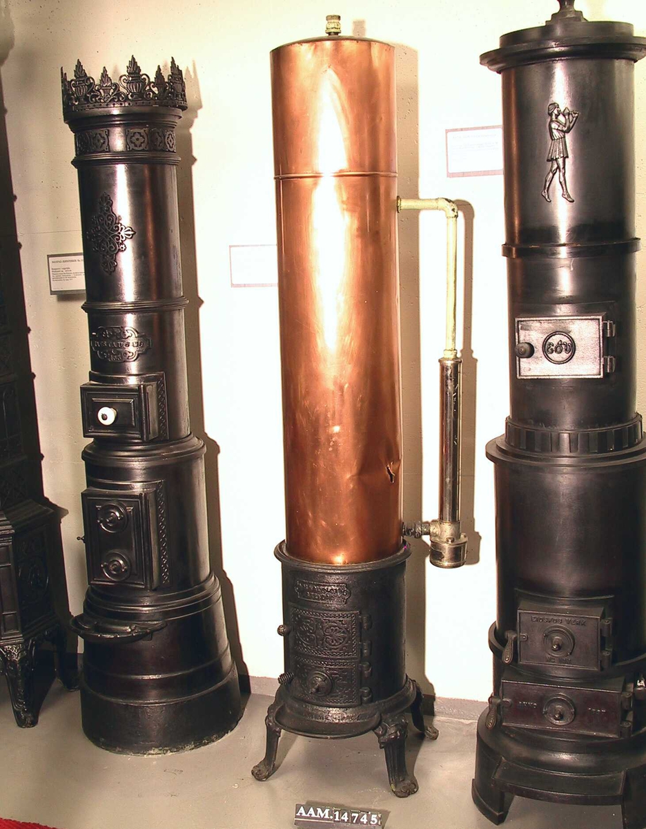 Varmtvannsovn for bad, badeovn. Støpejern, kobber  tank, forkrommet el. varmekolbe.  Mrk.   A M. Halvorsen, Arendal.  Ovn   Nedre del av støpejern,  sylindrisk m. glatte sider,  på 4 svungne skulpterte føtter. Ileg  2 hengslede  dører, nedre m. ventil, flatene m. skurd m.  palmetter og perlebord. over ilegget  påskrudd støpt  skilt m. rørleggerfirmaets navn. Profilert base og  gesims. Røkrøret fortsetter opp gjennom vanntanken  og munner ut bak.   Grov og stygg støpning.  Tank kobber, glatt. Svakt hvelvet  topp. Pusset og ripet, hull spalte på h. side ca. 4,51  og rundt hull til rør v. side nede, diam 3,5 cm.  Sylindrisk el. kolbe på h. side, firmamerke   Elektra, Oslo  senere påsatt, ant. 1930-40 årene.  Ledning mglr. Overflaten forkrommet. 