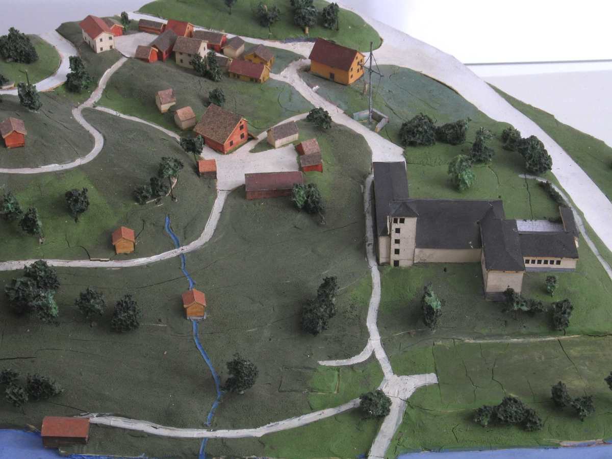 Plan og modell over Aust Agder Museet,  1952.   Furukasse  med   finerlokk,  I kassen en modell av Langsæterrenget,  med Barbuelva. Hovedbygningen fra 1858 er borte,  museumsbygget er større enn nå. Rundt i  terrenget spredte tun og bygate = Aust  Agder By og Folkemuseum (som omtalt bl. a.  i hefte 1934, Albert Uglands plan for museet).  