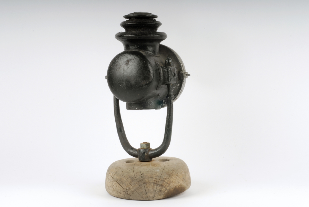 Form: Sylinderformet lykt med rundt glass i fronten.
Stativ av jern satt ned i foten. Oljedrevet til lampe før 1914 i Tyskland
