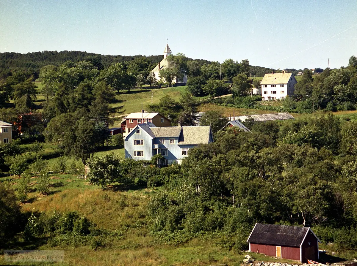 I midten er "lensmannsgarden" til Inge Hjertvik. .Naustet til Odd Hole i nerkant av bildet. .Husene bak tilhører Paul Breivik og Håkon Kvernberg (oppe til høyre). .I venstre kant skimtes konfeksjonsfabrikken til Øverås (som i dag er treningssenter).