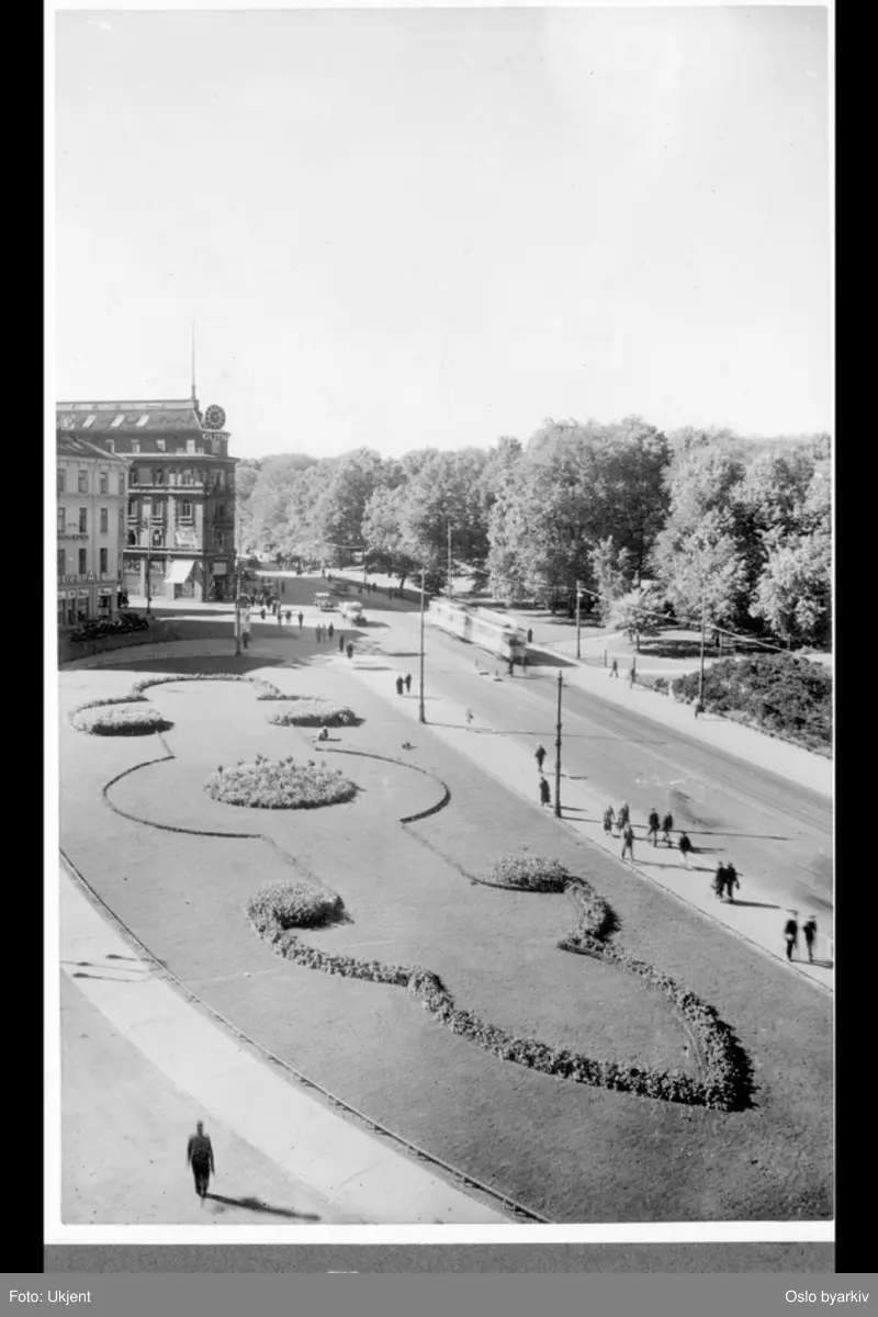 En blomsterbed- og plenprydet Triangelplassen (omdøpt 1962 til 7. juni plass) ved Drammensveien. Gatemiljø med spaserende og trikk. Krysset mot Kronprinsens gate i bakgrunnen. Søndre del av Slottsparken. (Bildetittel er misvisende, da Victoria terrasse er utenfor området) Albumtittel: "Vålerengen Viktoria" (terrasse)