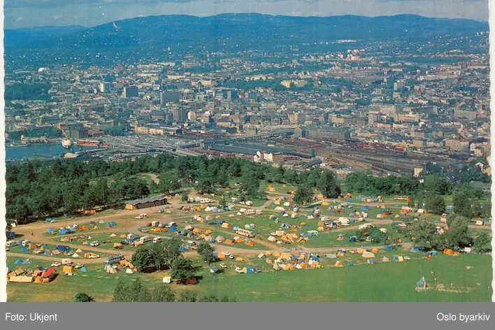 Ekeberg Camping ved Ekebergsletta, telt, campingvogner, biler, busser.  Ekebergskogen. Panorama over byen mot Holmenkollsen. Postkort. (Flyfoto)  -Oslo byarkiv / DigitaltMuseum