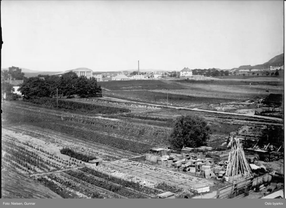 Fotografert mot nord fra taket på Østre Hasle gård i Økernveien. Den store hallen med buet tak til venstre er Norsk Motor-og Dynamofabrik (senere Per Kure A/S), anlagt på stedet i 1913.Til høyre for denne ligger Fellesslakteriet, anlagt her i 1911. Til høyre bak skogholtet skimtes taket på låven på Løren gård. Mer detaljert informasjon om motivet finnes.