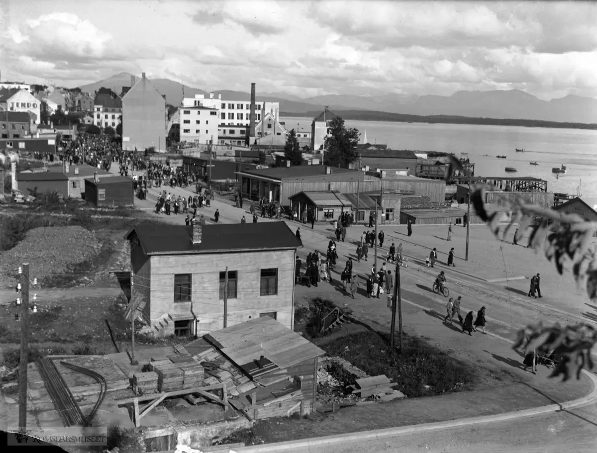 Kronprins Olav på besøk i Molde 27.juli 1945. I bakgrunnen ses Helseth-huset til venstre foran "tempo" Helset huset var det eneste huset som overlevde bybrannen 1916 og brannen 1940, Gotfred Lies plass med konfektionsfabrikken, Meieriet og telegrafen ses også i bakgrunnen. Torget er nede til høyre.