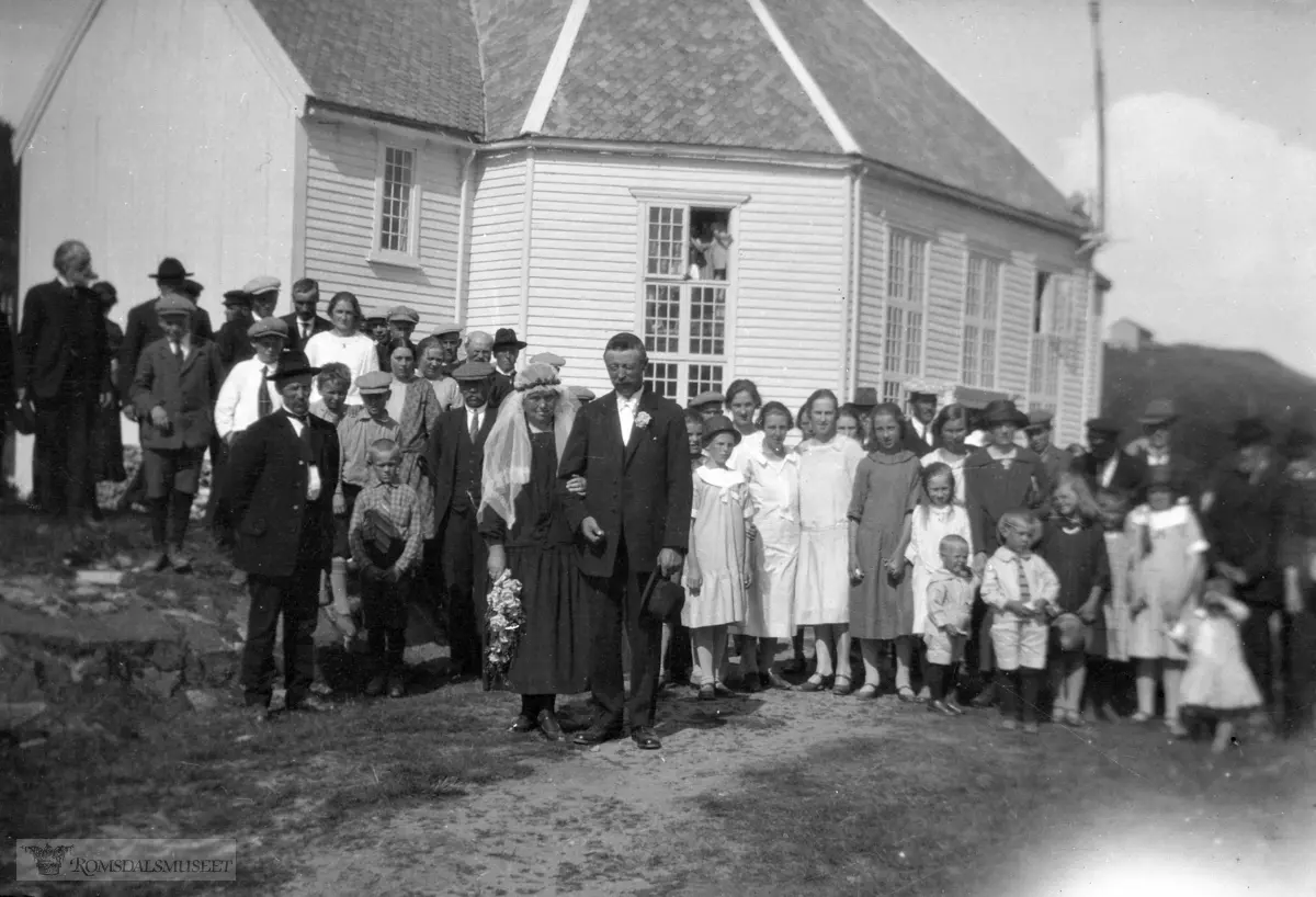 Brudefølge ved Kleive kirke., Bryllupet til Marit Mauset, f. 1883 - d. 1976 og Peder P. Ulleland fra Oppigarden. f. 1877 - d. 1954.Viet i Kleive kirke 1927..."Bruden 44 år og brudgommen 50 år..Peder eide gården Ulleland Øvre (Oppigarden) som han drev sammen med sin.bror Anders f. 1879 d. 1945...Som ung jente var Marit i tjeneste hos Peders søster Ellen Anna Ytterhaug..Senere reiste Marit, som så mange andre jenter i bygda, til Oslo for å tjene..Hun var kokke i flere såkalt ”finere” familier bl.a. hos Lorentzen. .En venninde var kokke hos familien Astrup. .Marit reiste tilbake til bygda Kortgården og giftet seg med Peder i 1927...For flere generasjoner tilbake ble hovedgården Ulleland delt i 3:.1..Ulleland Nedre, på folkemunne kalt Nerigarden..2..Ullelandsmyran, (hjemmet til fotografen) ble kalt Myran..3..Ulleland Øvre, ble omtalt som Oppigarden - gårdsnr. 94/ bruksnr. 3.Marit og Peder fikk ingen barn..I 1950 overførte Peder gården til sin søstersønn Asbjørn Ytterhaug, gift med .Synnøve Louise Holsbø. .De overtok gården i 1954.".Løa på Skalde kan ses på haugen til høyre bak kirka..(bilder fra konvolutt merket "filmer fra 1927")