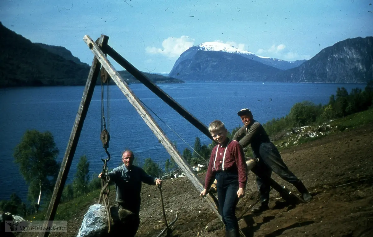 Gridset (Griset), Larsgarden, gnr. 95/2, Rauma kommune. Jordbryting. Dei fjernar ein stein med stubbebrytar. Til venstre stikk Hovde-grenda ut i Romsdalsfjorden. Vidare Oksen og Høgberga med Nordvika mellom seg..Bildet er truleg frå 1966-67.."Sommerens brennpunkt 1978"