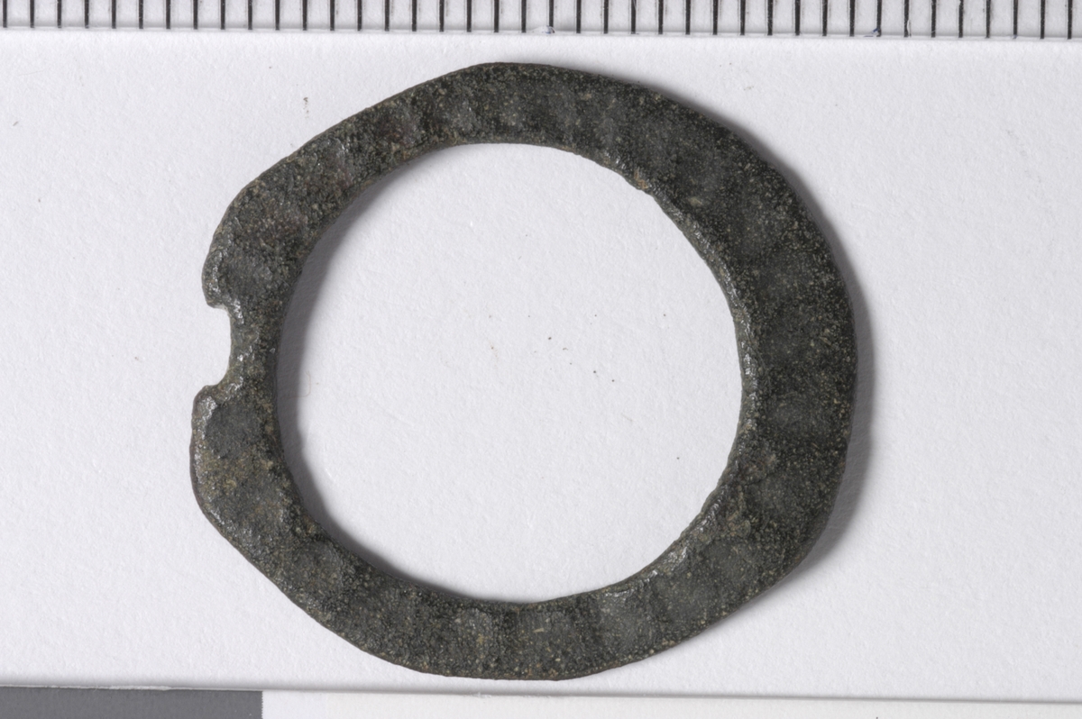 MALV: DIAM. 23  ST. B 5 MM, RINGFORMET, LAGET AV FLATT 3-5 MM BREDT BÅND. REKTANGULÆRT UTTAK FOR TORNEN SOM MANGLER. DEN ENE SIDEN HAR RADIALERIFLER. 