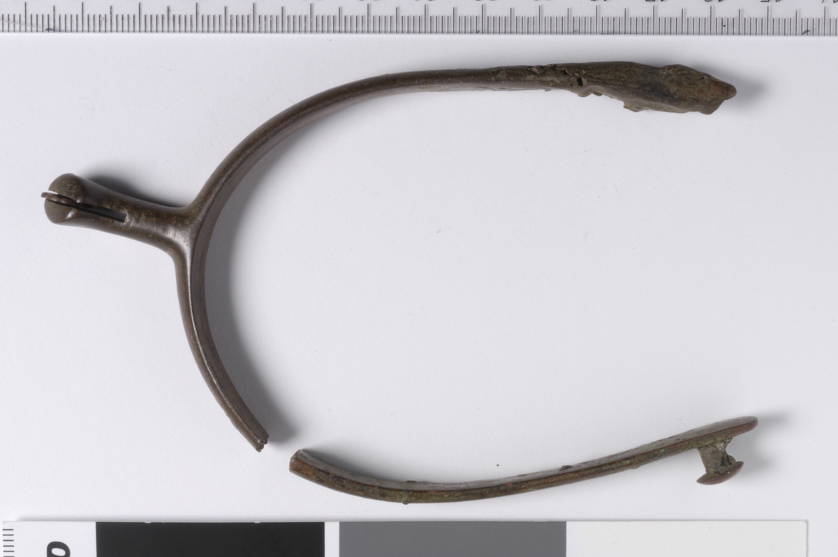 MALV: H. 18 MM  B. PÅ ARM 10 MM, ARMEN OG HJULFESTET TILNÆRMET I SAMME PLAN. DEN ENEARM HAR EN KNOTT PÅ ENDENS UTSIDE, DEN ANDRE ARM ER ØDELAGT. ET LITE"HJUL" SITTER SITTER IGJEN I SPALTEN. ER DETTE SPORE F. NYERE TID ?