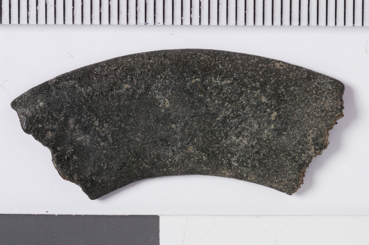 En avlang og buet metallplate med et tverrsnitt som buer svakt i kantene. Overflaten er glatt og baksiden mer ru. Gjenstandern har bruddflater i begge ender og ingen tegn til dekor. Dette er del av et rundt beslag, men med ukjent bruksområde.
