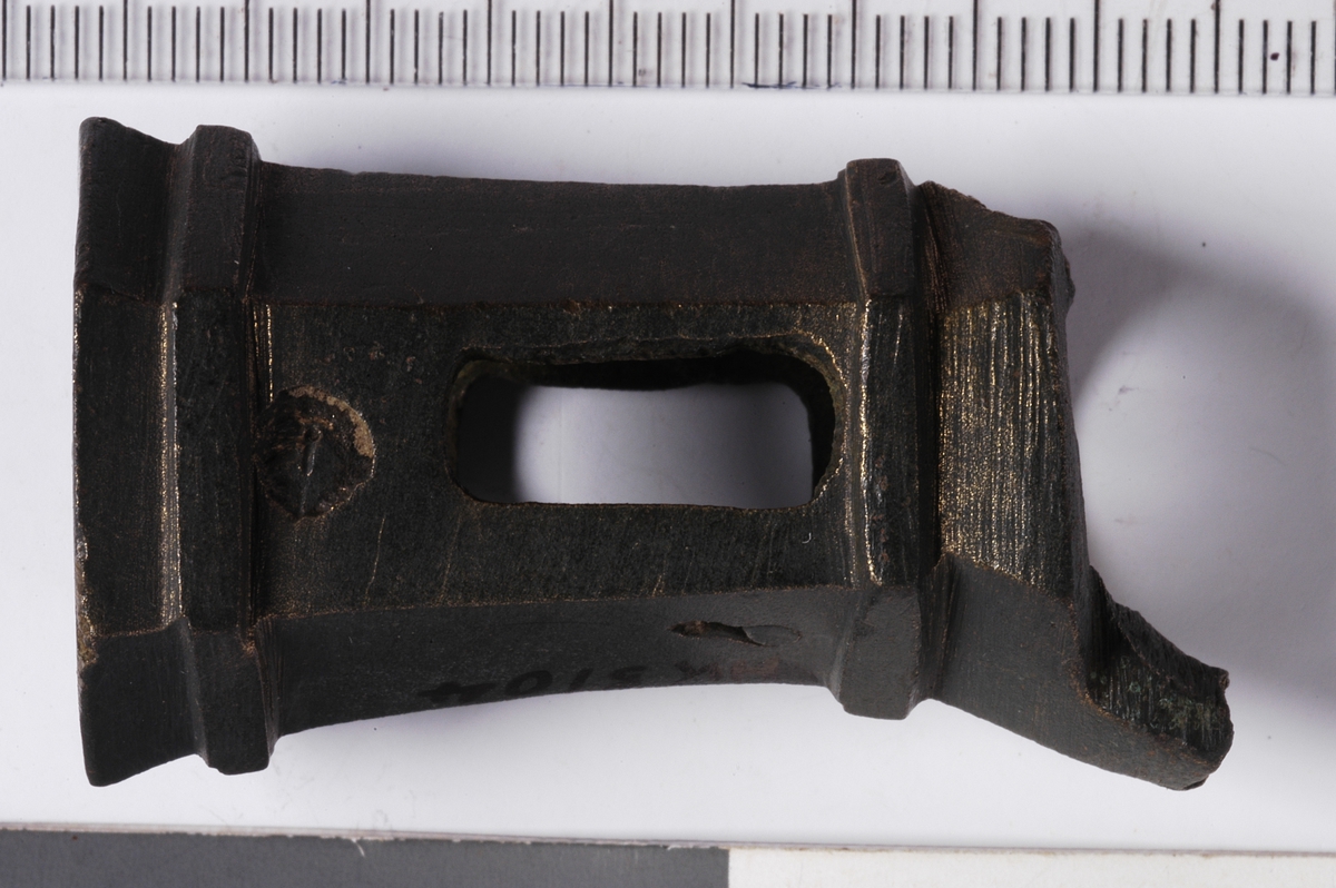 MALV: H. 44 MM  DIAM. 23 MM, SEKSKANTET, DOBBELTKONISK MED TO FLATE BÅND OPPE OGNEDE. ÅPNING I HVER ENDE. TO RETT OVERSTILTE TILNÆRMET REKTANGULÆREHULL NOE NEDENFOR MIDTEN. TO AVBRUKNE FESTER ETTER BEN - AV DET ENEGJENSTÅR ET LITE STYKKE SOM ANTYDER EN BRENT FORM. 
