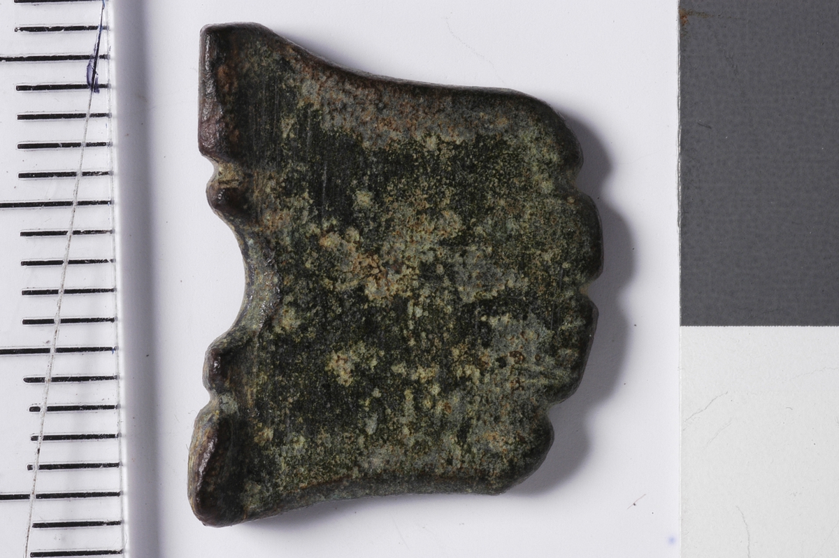 Tilnærmet firkantet gjenstand med en halvsirkelformet fordypning i den tykkeste enden. Denne enden fungerer som en "fot" som gjør at gjenstanden står stabilt oppreist. Tykkelsen er avsmalnende opp fra foten. Alle sider er intakte og toppen, dvs motsatt ende av foten, er bearbeidet med tre fordypninger som gir en bølgeform. Midt i overflaten av gjenstanden, rett over buen, sees på den ene siden rester av en fordypning som kan ha vært et preg. Kan være en spillebrikke.