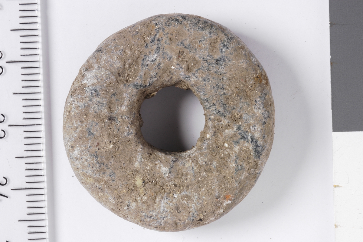 Et spinnehjul i stein med flat under og overside, samt svakt buede ytterkanter.